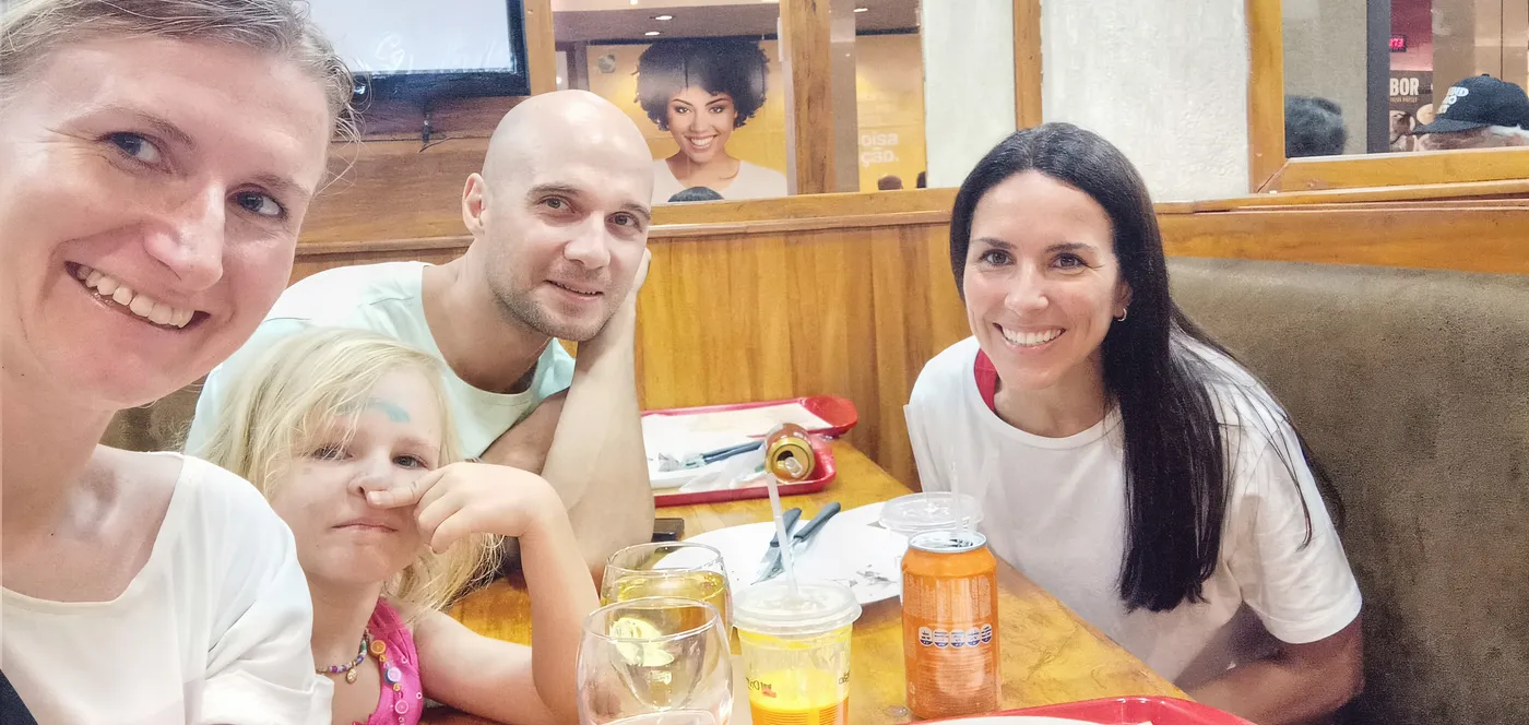 Patrícia sorrindo ao lado de uma família de alunos estrangeiros em um restaurante